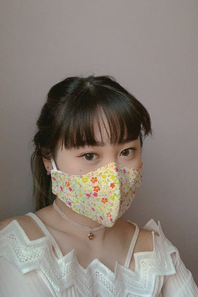 a model wearing a warm toned mask reminiscent of spring with a green, yellow, orange, and magenta flower print