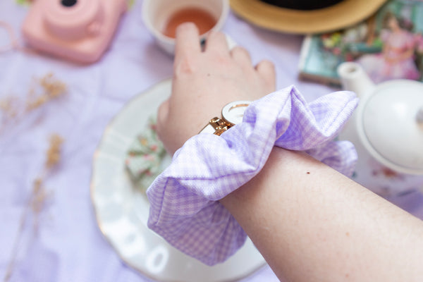 a purple and white gingham print scrunchie worn on a wrist