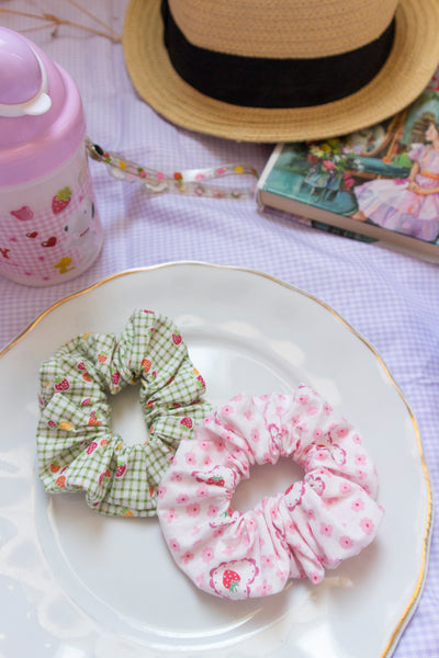 a green plaid scrunchie and pink scrunchie on a plate in a picnic setting