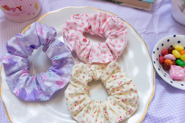 a purple scrunchie, pink scrunchie, and yellow scrunchie placed on a plate in a picnic setting