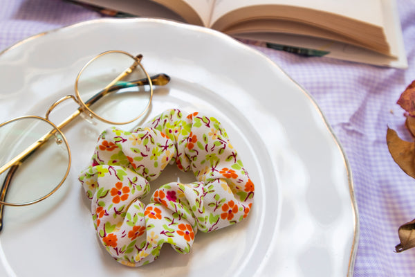 a warm toned scrunchie reminiscent of spring with a green, yellow, orange, and magenta flower print